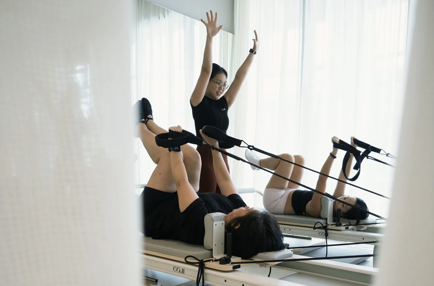 A Goji physiotherapist guiding two clients through a reformer Clinical Pilates session.