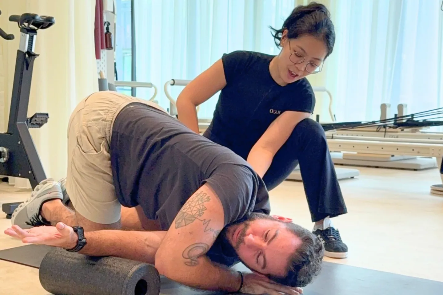 A Goji physiotherapist guiding a man through a mobility stretch on a mat beside a foam roller